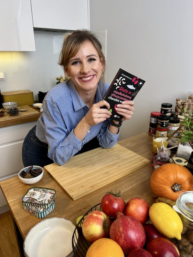 Dietetyk Klaudia Wiśniewska prezentuje swoją książkę o zdrowym żywieniu. Na zdjęciu widać różnorodne warzywa i owoce, które są podstawą zbilansowanej diety.